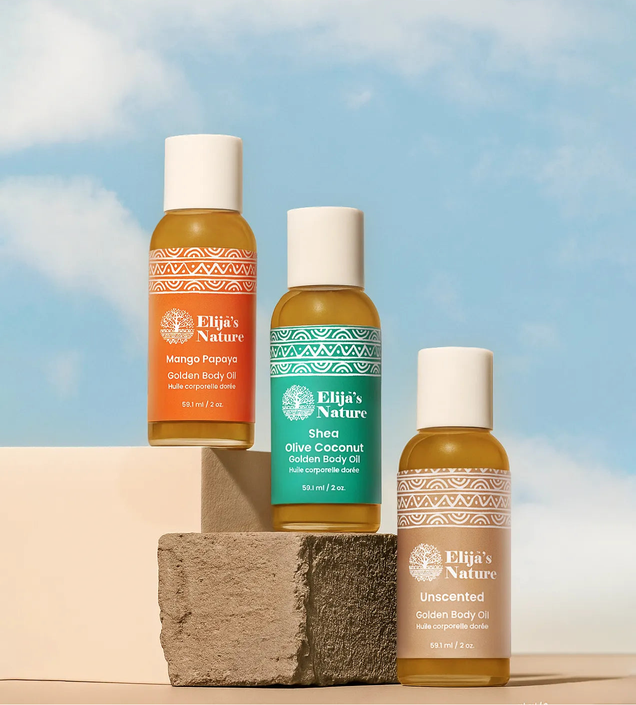 Heavenly Trio Gift Set - #size_2oz - Mini bottles of Elija’s Nature Mango Papaya, Olive Coconut, and Unscented body oils arranged on clay blocks against a bright blue sky