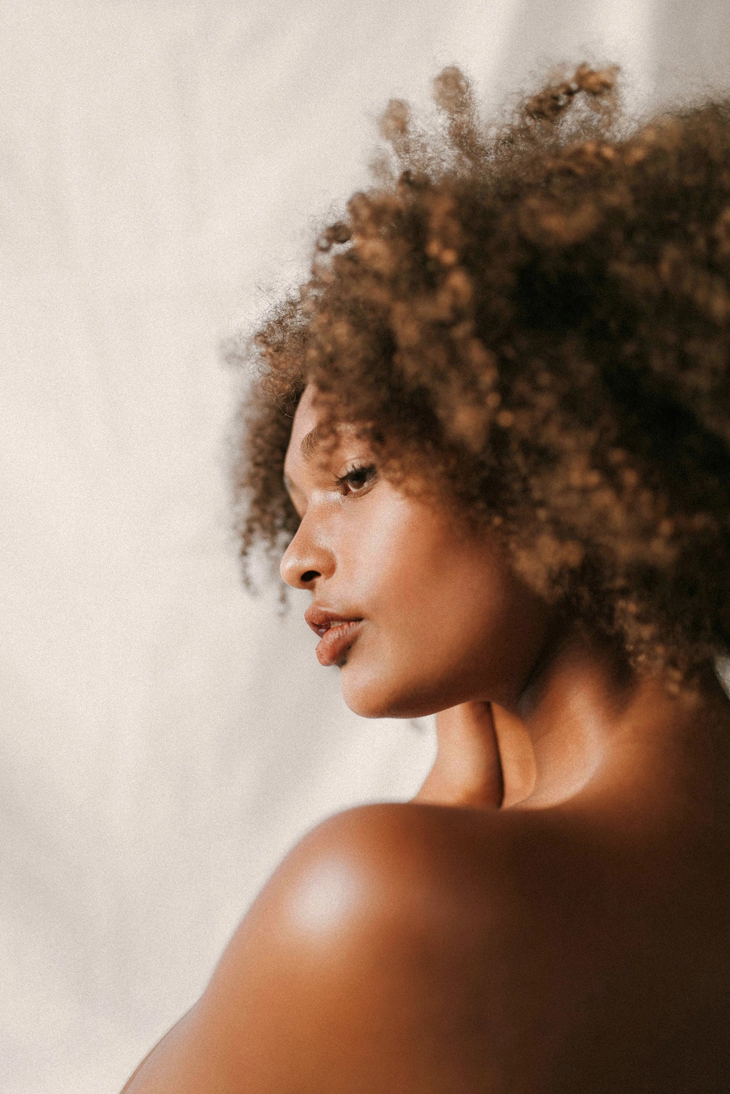 Portrait of a woman with curly hair looking to the side, softly lit against a neutral backdrop