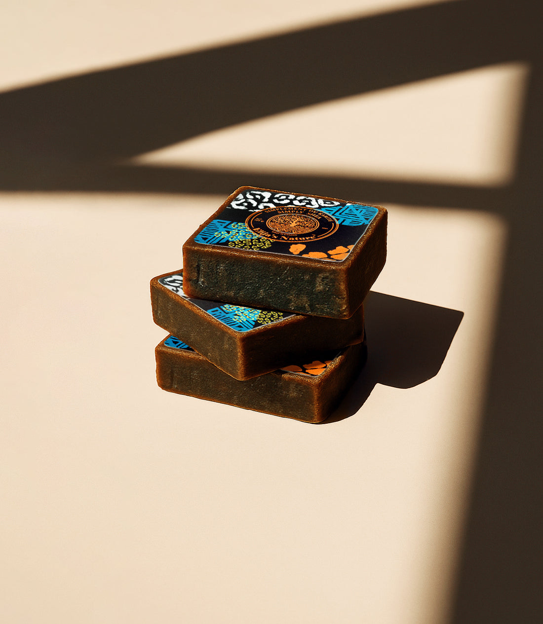 Stack of three Elija’s Nature Black Soap Bars with patterned labels, arranged on a beige surface with bold shadow lines