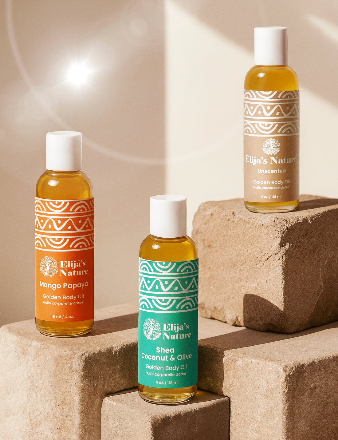 Three Elija’s Nature body oil bottles, Mango Papaya, Olive Coconut and Unscented arranged on textured beige stone blocks under soft studio lighting