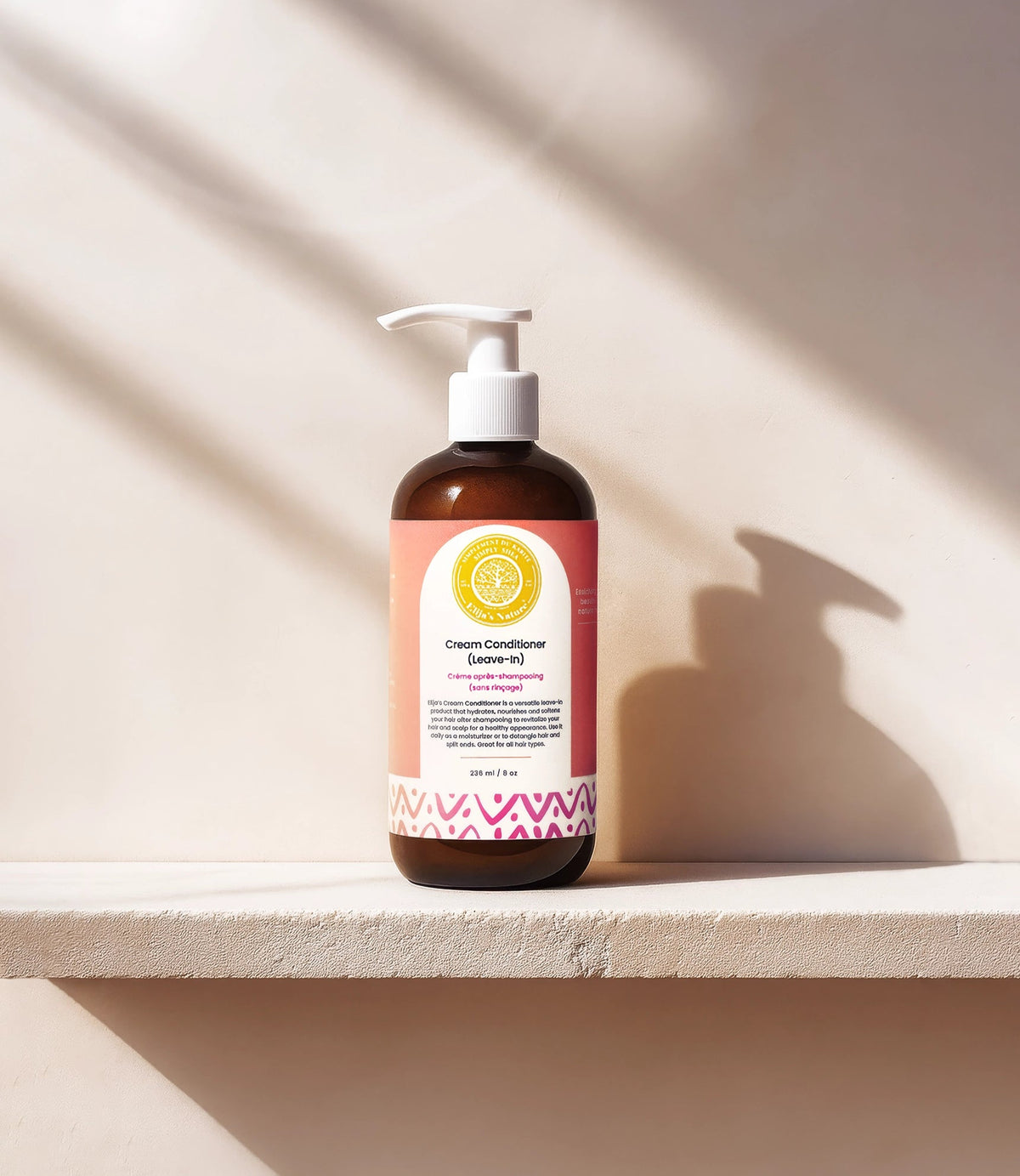 Cream Conditioner Leave-In - #size_8oz - Bottle of Elija’s Nature Cream Leave-In Conditioner standing on a white ledge, casting a strong shadow against a beige wall