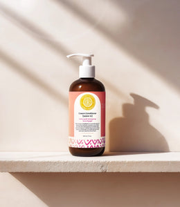 Cream Conditioner Leave-In - #size_8oz - Bottle of Elija’s Nature Cream Leave-In Conditioner standing on a white ledge, casting a strong shadow against a beige wall