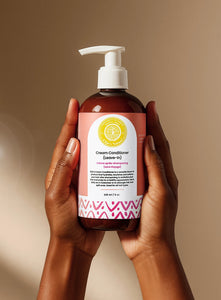 Cream Conditioner Leave-In - #size_8oz - Hands holding a bottle of Elija’s Nature Cream Leave-In Conditioner upright against a neutral background