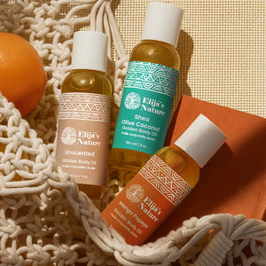 Heavenly Trio Gift Set - #size_2oz - Three Elija’s Nature body oil bottles: Unscented, Olive Coconut, and Mango Papaya placed in a woven bag with an orange on a warm-toned surface