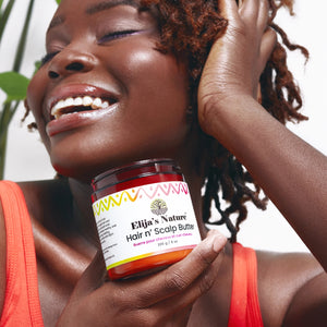 Hair N Scalp Butter - #size_8oz - Smiling woman with textured hair holding Elija’s Nature Hair n’ Scalp Butter jar beside her face, surrounded by greenery