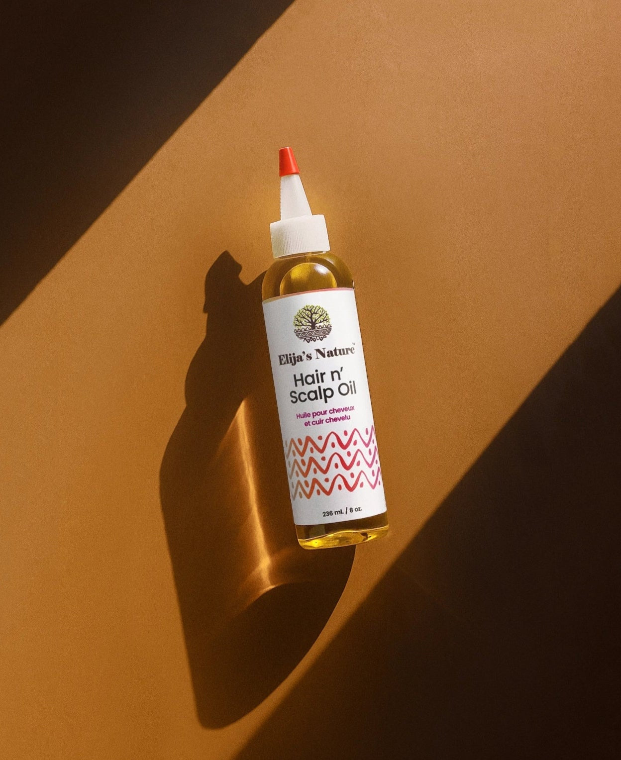 Hair N' Scalp Oil - #size_8oz - Elija’s Nature Hair n’ Scalp Oil bottle lying diagonally on a warm brown surface with strong directional light and shadow