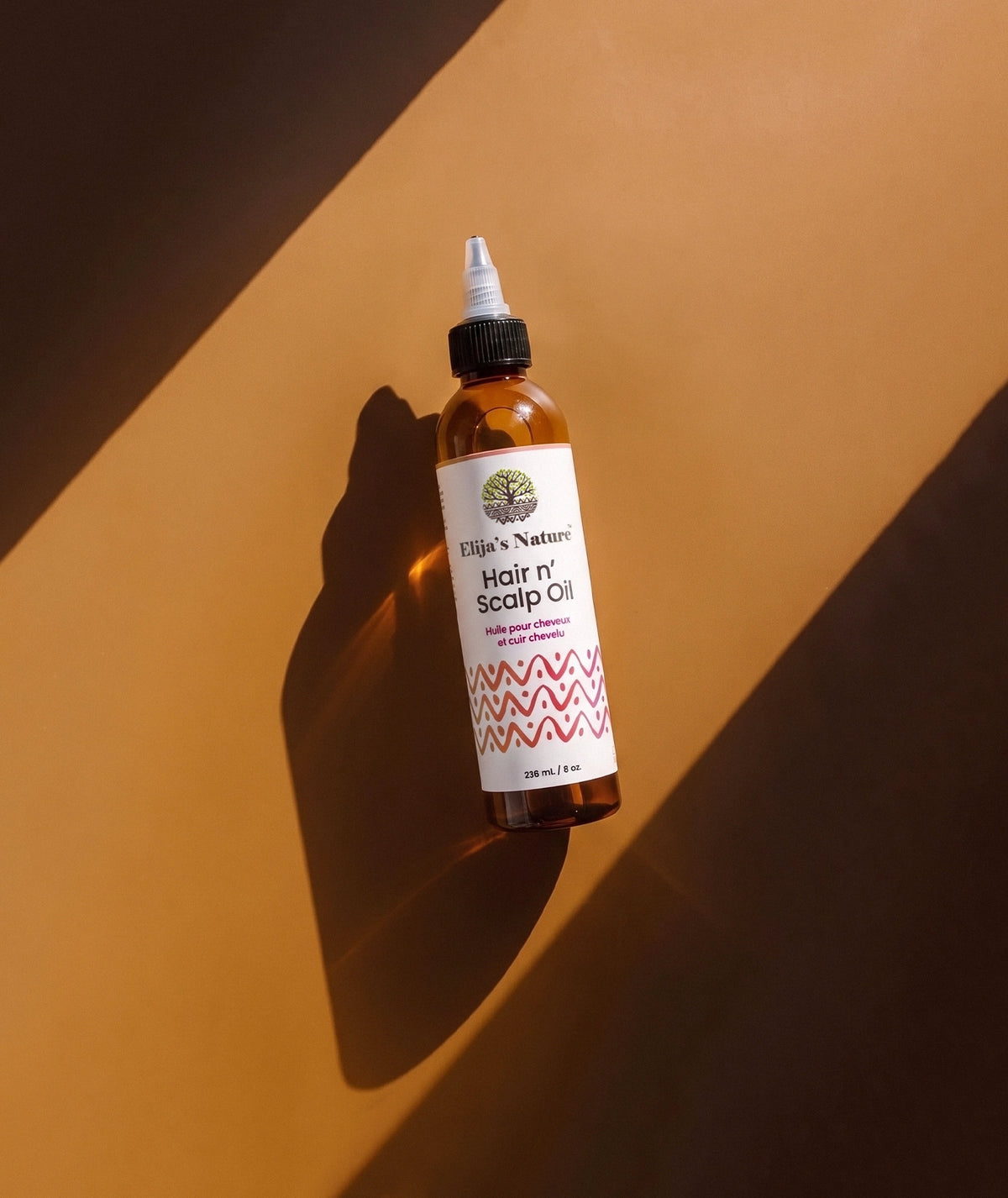 Hair N' Scalp Oil - #size_8oz - Elija’s Nature Hair n’ Scalp Oil bottle lying diagonally on a warm brown surface with strong directional light and shadow