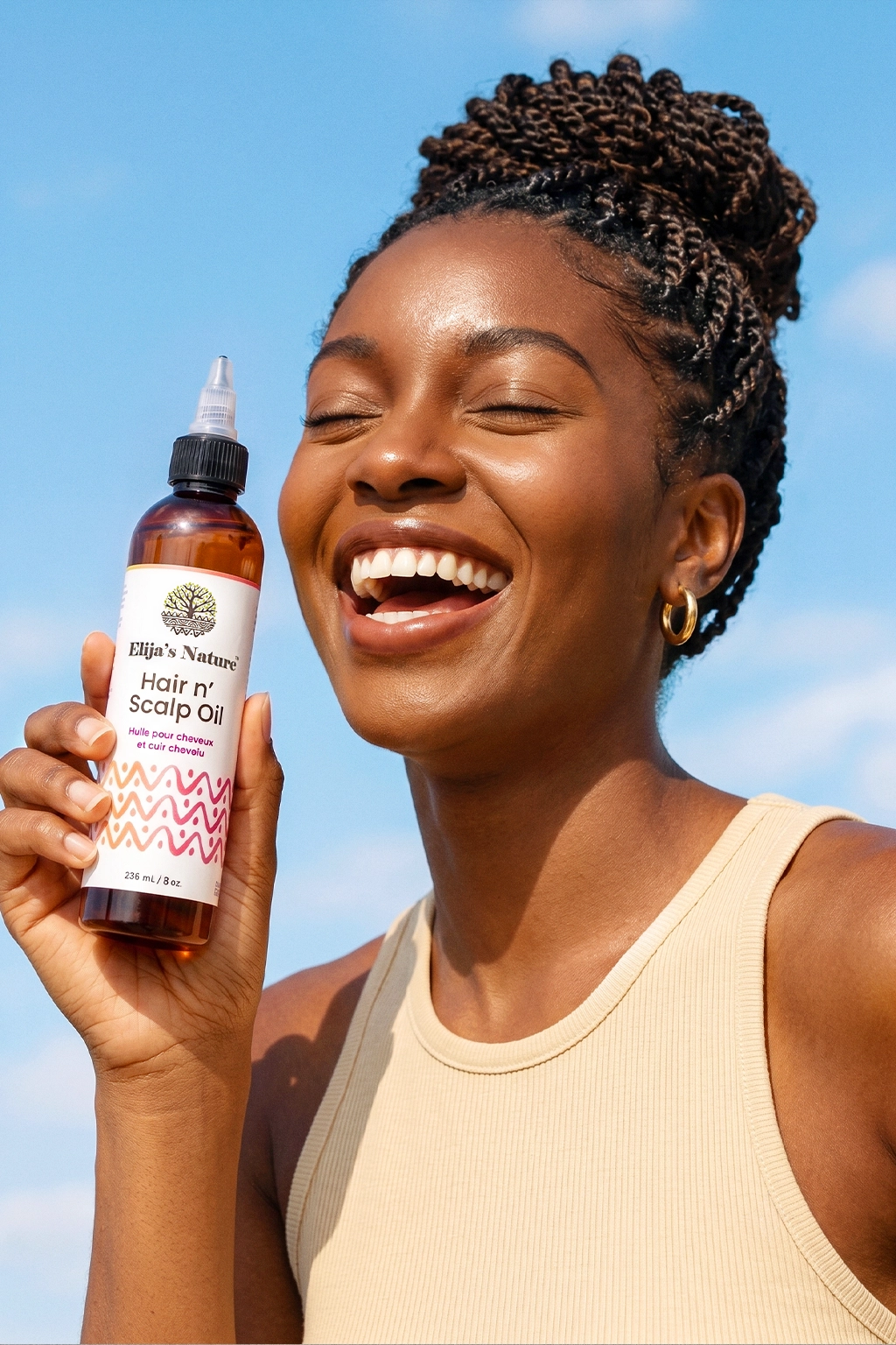Hair N' Scalp Oil - #size_8oz - Woman with braided hair smiling and holding Elija’s Nature Hair & Scalp Oil bottle in front of a blue sky