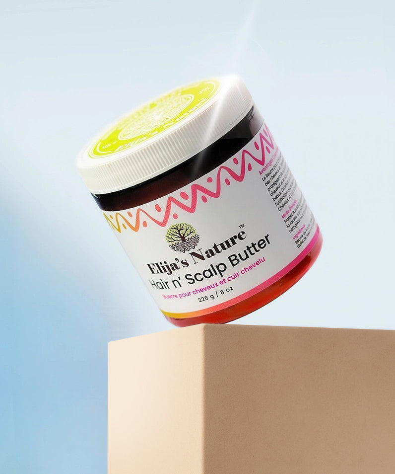 HairNButterScalp Packshot - #size_16oz - Elija’s Nature Scalp Butter jar balanced on a beige pedestal against a pastel blue background, with the product tilted to reveal the label and lid design under soft lighting