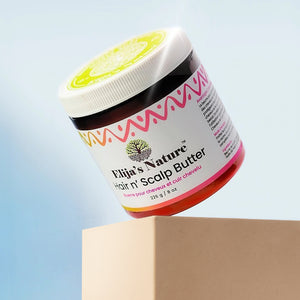 HairNButterScalp Packshot - #size_16oz - Elija’s Nature Scalp Butter jar balanced on a beige pedestal against a pastel blue background, with the product tilted to reveal the label and lid design under soft lighting