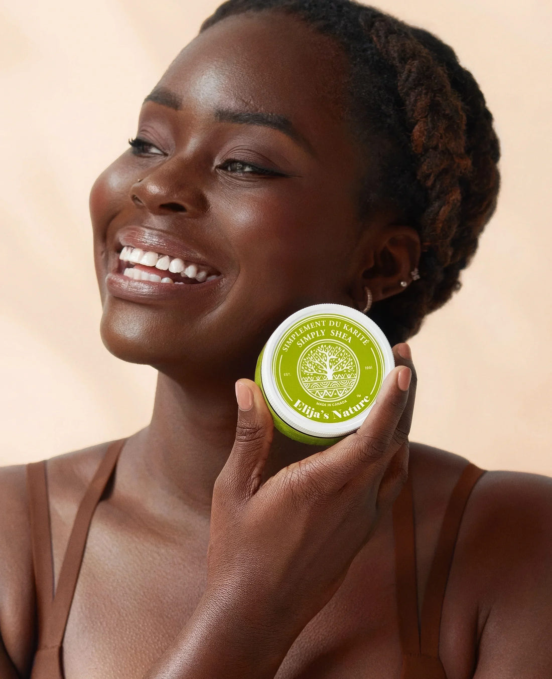 Smiling woman holding a Lemon Blossom jar of Elija’s Nature Golden Body Butter 8oz near her face