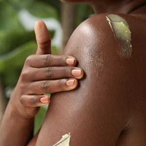 Golden Body Butter - #scent_Lemon Blossom - A close-up of a woman gently applying a yellow-tinted body butter to her shoulder, suggesting targeted nourishment and a botanical formula