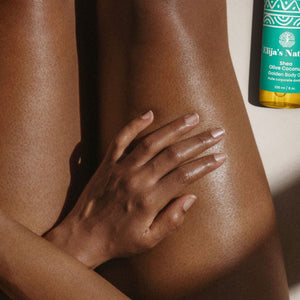 #scent_Olive Coconut #size_8oz - Woman with glowing skin sitting next to an Elija's Nature Golden Beauty Oil in the scent Olive Coconut