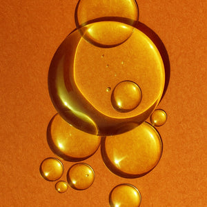 Close-up of golden oil drops on an orange background representing Elija’s Nature Golden Body Oil